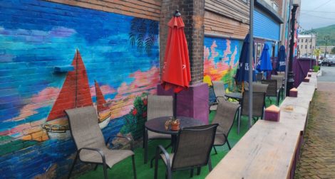 Outdoor restaurant seating with a colorful mural behind the chairs and tables 